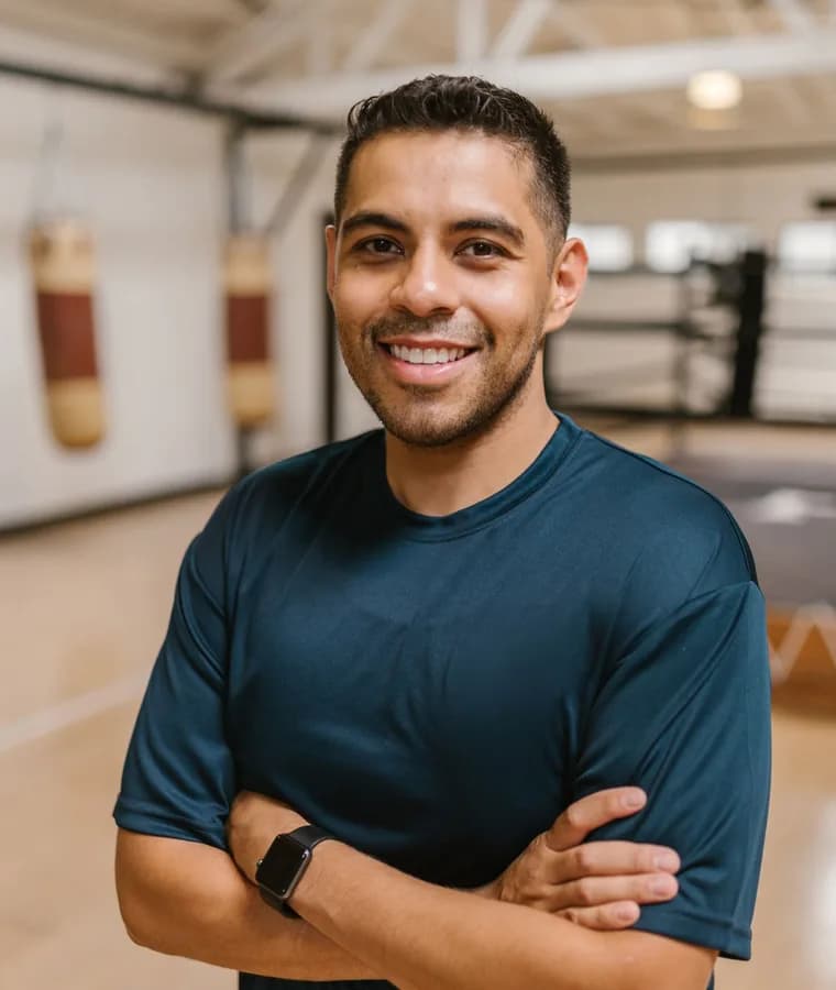 Personal trainer sorrindo, de braços cruzados, no estúdio de treino