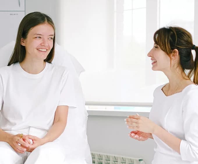 Profissional de estética e cliente conversando e sorrindo na cabine da clínica