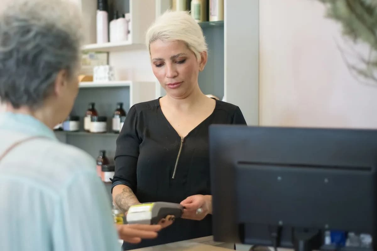 Profissional de salão passando a maquininha de cartão para a cliente no balcão