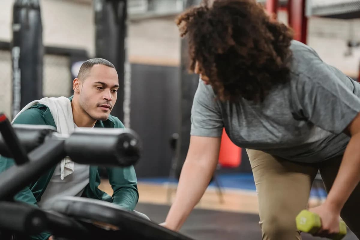 Personal trainer acompanhando de perto uma aluna em exercício com halter na sala de treino
