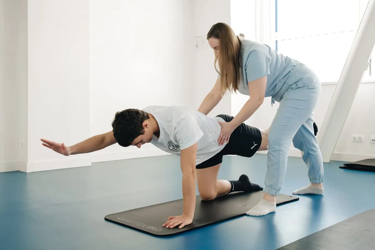 Fisioterapeuta corrigindo a postura de um paciente em exercício de reabilitação sobre o tatame